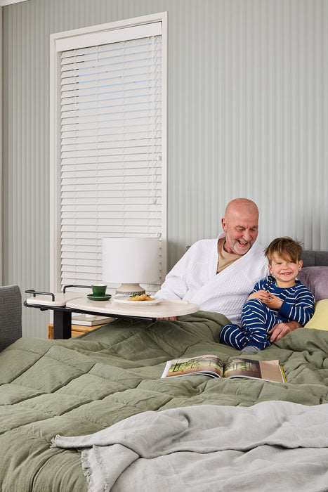 An older man and a child sitting together on a bed with a breakfast tray